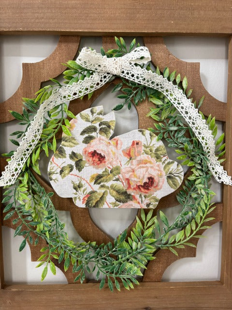 Decorative wreath with floral bunny and lace ribbon in a wooden lattice panel.