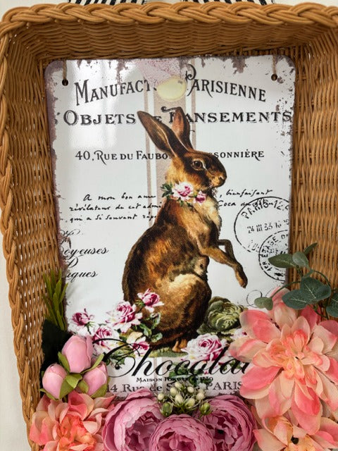 Decorative wall hanging with a rabbit illustration and floral elements, framed in wicker.