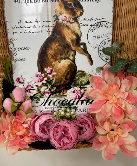 Decorative wall hanging with a rabbit illustration and floral elements, framed in wicker.