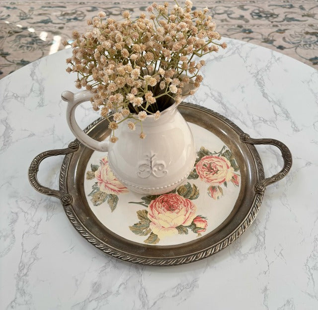 White pitcher with flowers on a decorative tray on a marble surface