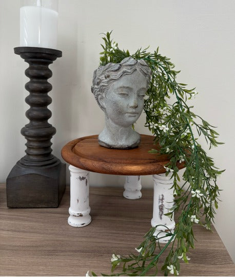 Decorative head sculpture on a small wooden riser with a candle and greenery in the background.