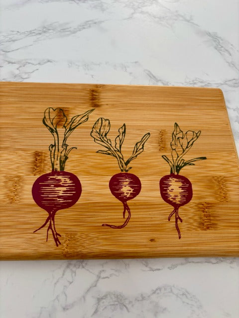 Wooden cutting board with stenciled radish designs on a marble surface