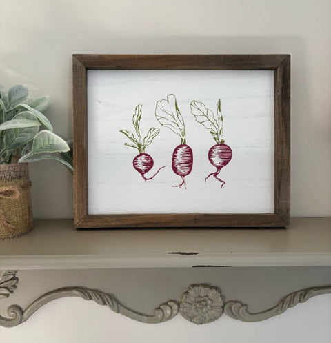 Framed artwork of radishes on a decorative shelf with a plant in the background