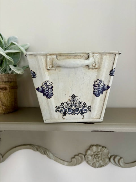 Decorative metal basket with blue floral patterns on a shelf.
