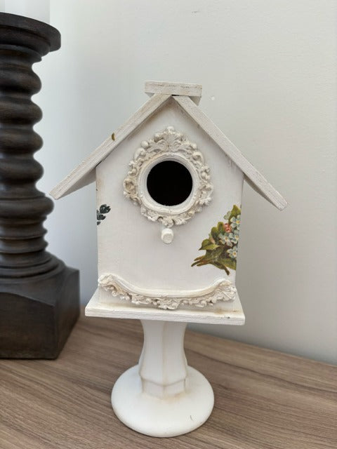 Decorative white birdhouse with floral designs on a glass base