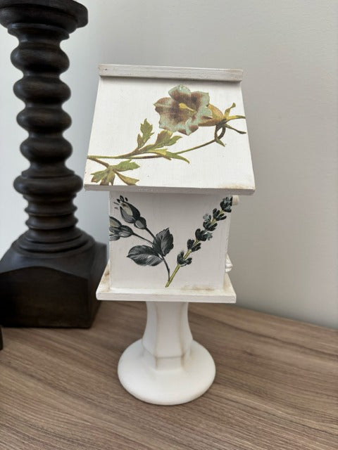 Decorative white birdhouse with floral designs on a glass base