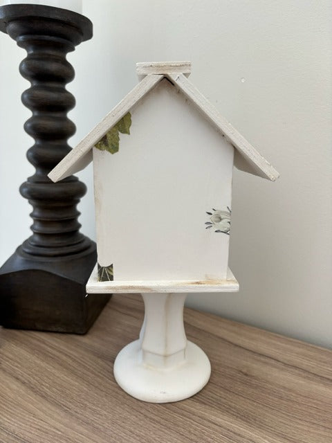 Decorative white birdhouse with floral designs on a glass base