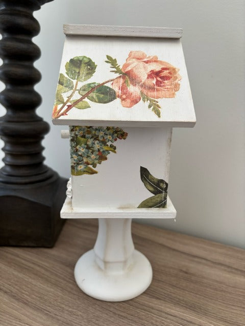 Decorative white birdhouse with floral designs on a glass base