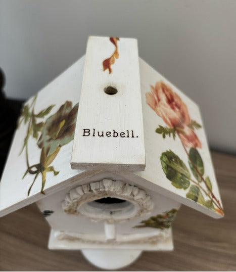 Decorative white birdhouse with floral designs on a glass base