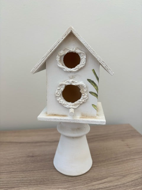 Decorative white birdhouse with floral designs on a glass base