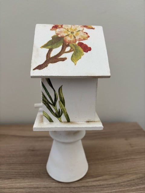 Decorative white birdhouse with floral designs on a glass base