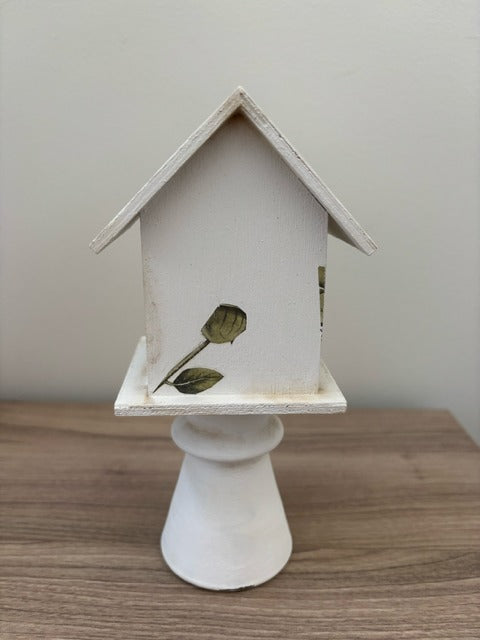 Decorative white birdhouse with floral designs on a glass base