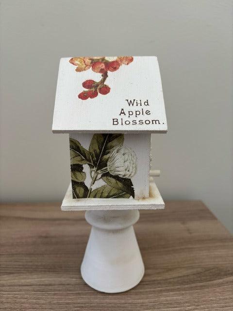 Decorative white birdhouse with floral designs on a glass base