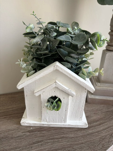 White birdhouse-shaped planter with greenery 