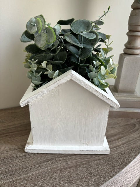 White birdhouse-shaped planter with greenery 