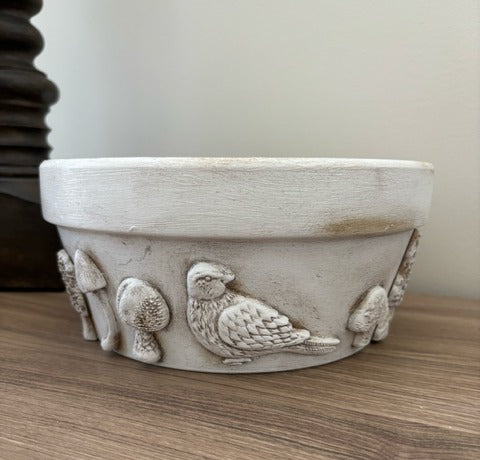 Decorative ceramic bowl with bird and mushroom designs on a wooden surface