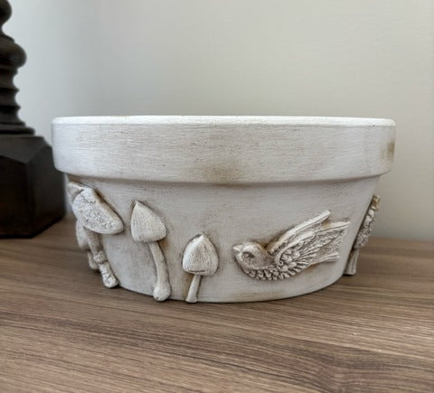 Decorative ceramic bowl with embossed designs of mushrooms and a bird on a wooden surface.