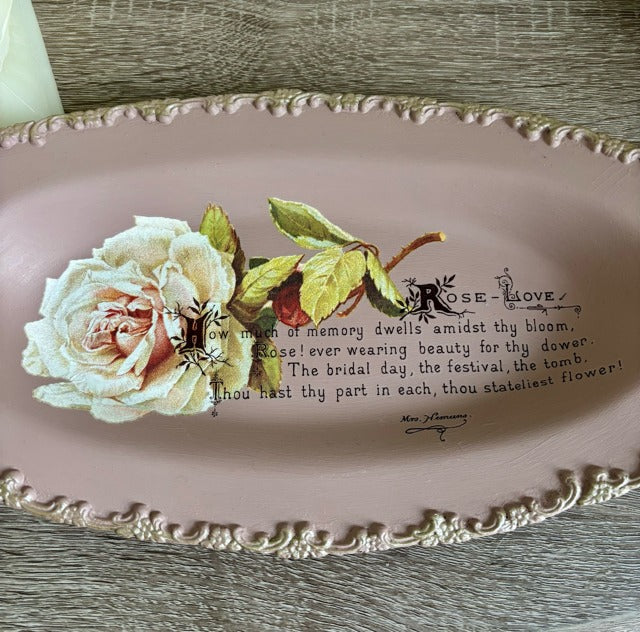 Decorative plate with a rose design and text on a wooden surface