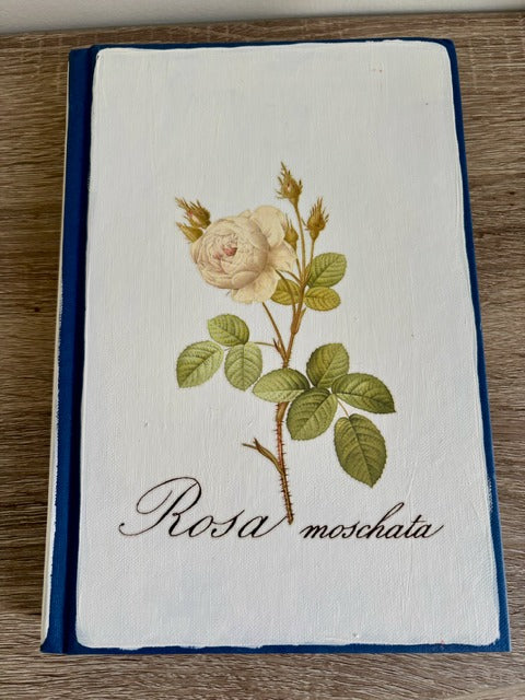 Book with embroidered rose design and 'Rosa moschata' text on a wooden surface