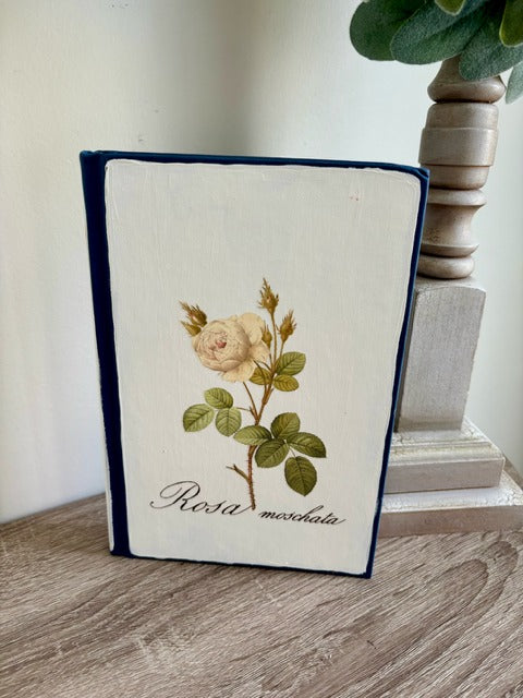 Book with floral design and 'Rosa moschata' text on a wooden surface
