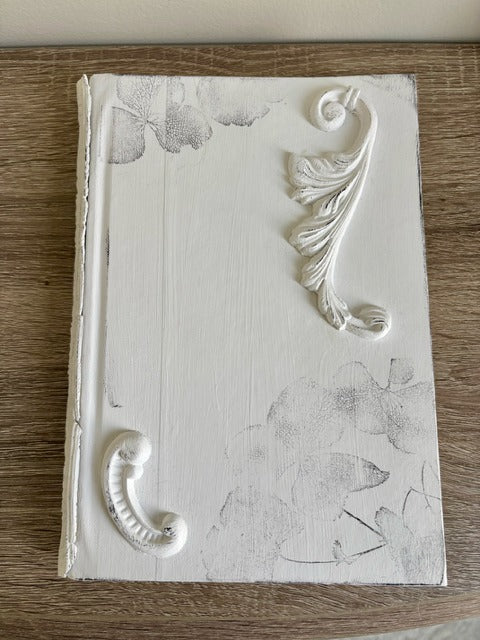 Decorative white book with leaf designs on a wooden surface