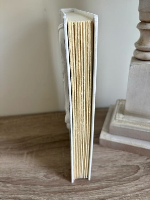 White book with beige pages standing upright on a wooden surface.