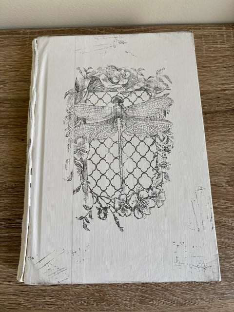 Book with decorative cover featuring a dragonfly design on a wooden surface