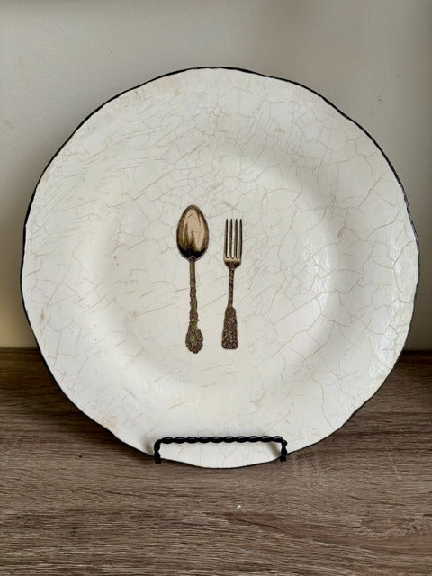White ceramic plate with crackled texture and spoon and fork design on a wooden surface.