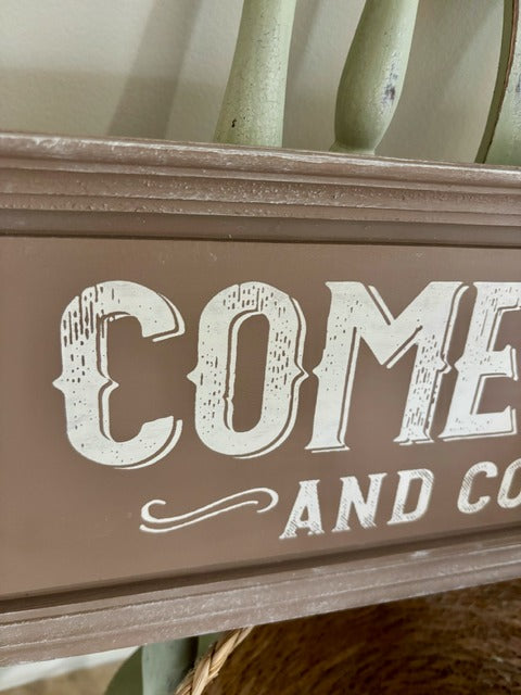 Decorative sign with 'Come and Stay' text on a wooden frame.