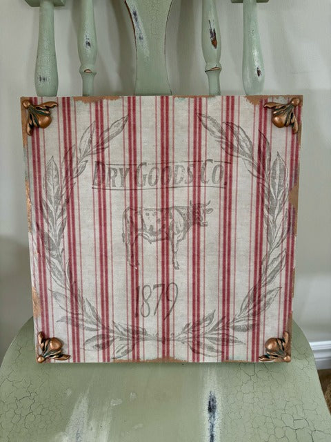 Decorative sign with red and white striped pattern and cow illustration on a green surface.