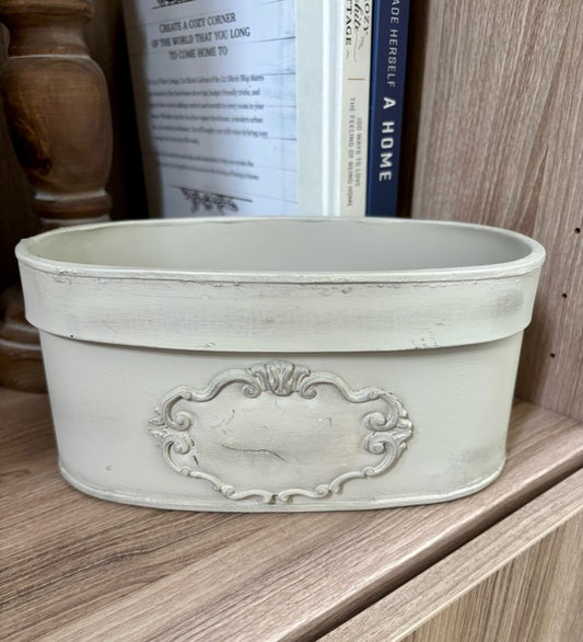 Decorative oval planter with intricate design on a wooden shelf