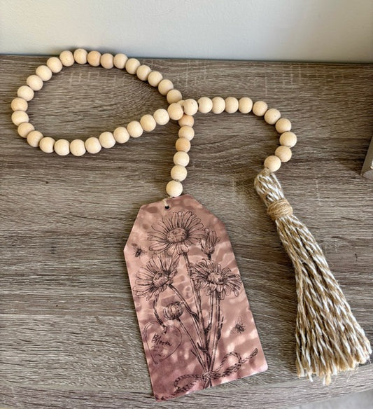 Wooden beaded garland with a floral tag and tassel on a wooden surface