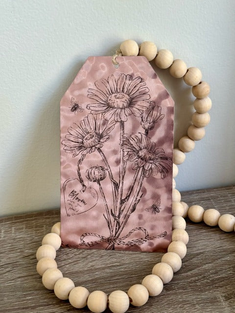 Decorative garland with floral design on a pink background, framed by wooden beads.