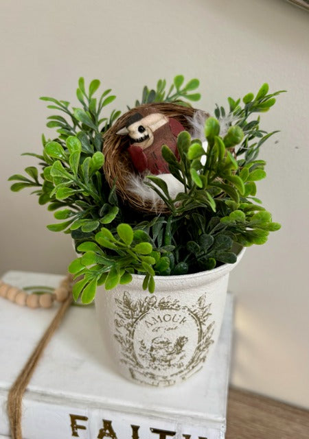 Decorative arrangement with greenery and a bird figurine in a white container.