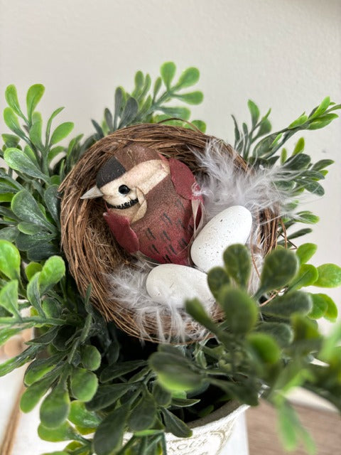 Decorative arrangement with greenery and a bird figurine in a white container.