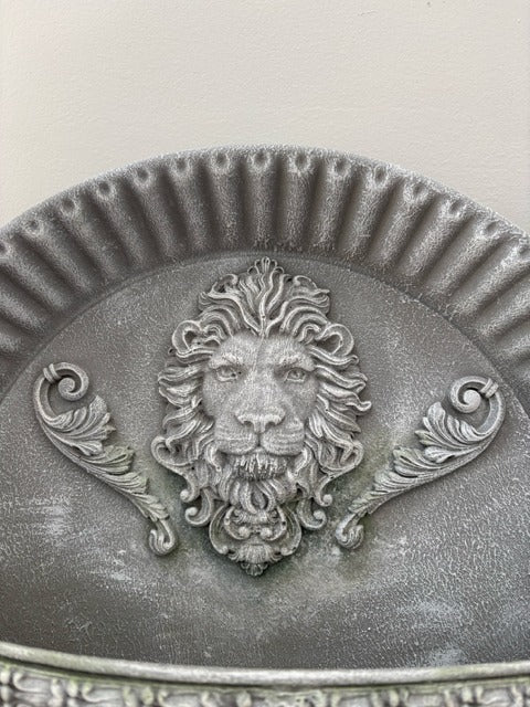 Decorative metal wall piece with a lion's head design on a textured background