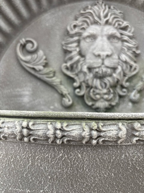 Decorative metal object with a lion's head and decorative elements on a textured surface