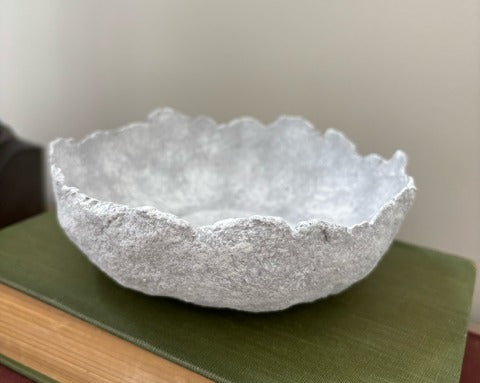 Textured paper mache bowl on a green surface with a neutral background