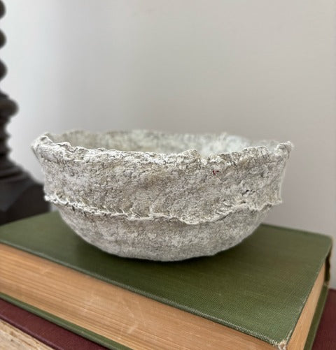 Textured paper mache bowl on a green book with a plain background