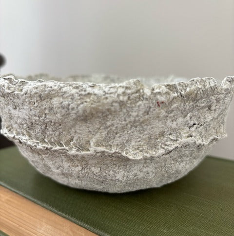 Textured paper mache bowl on a green surface with a neutral background